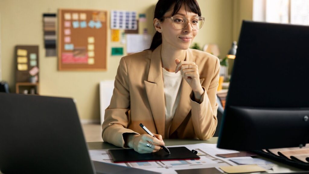 Salon owner working on a computer while reviewing business plans and financial documents at an office desk.