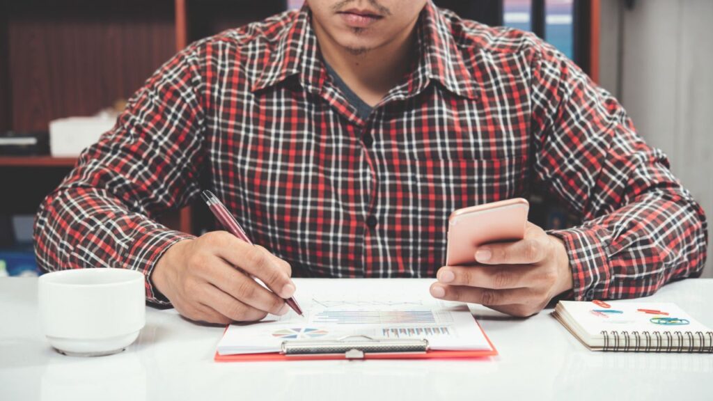Small business owner reviewing financial reports and expenses on a smartphone while managing tax planning and business finances.