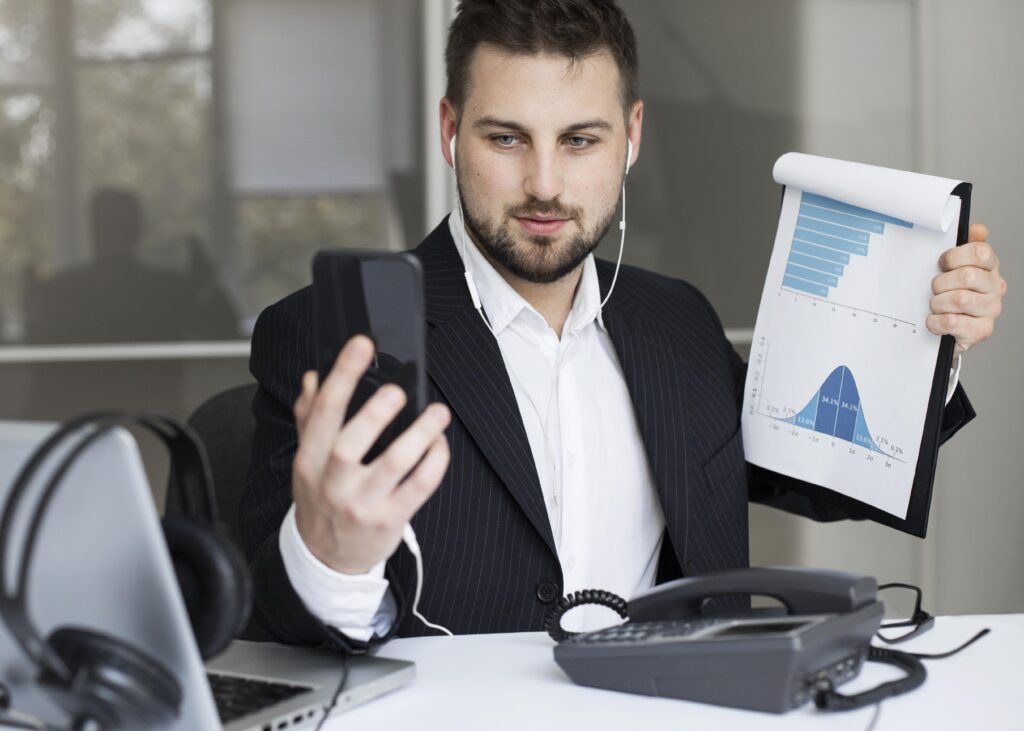 Businessman wearing earphones showing clipboard charts during a smartphone video call.