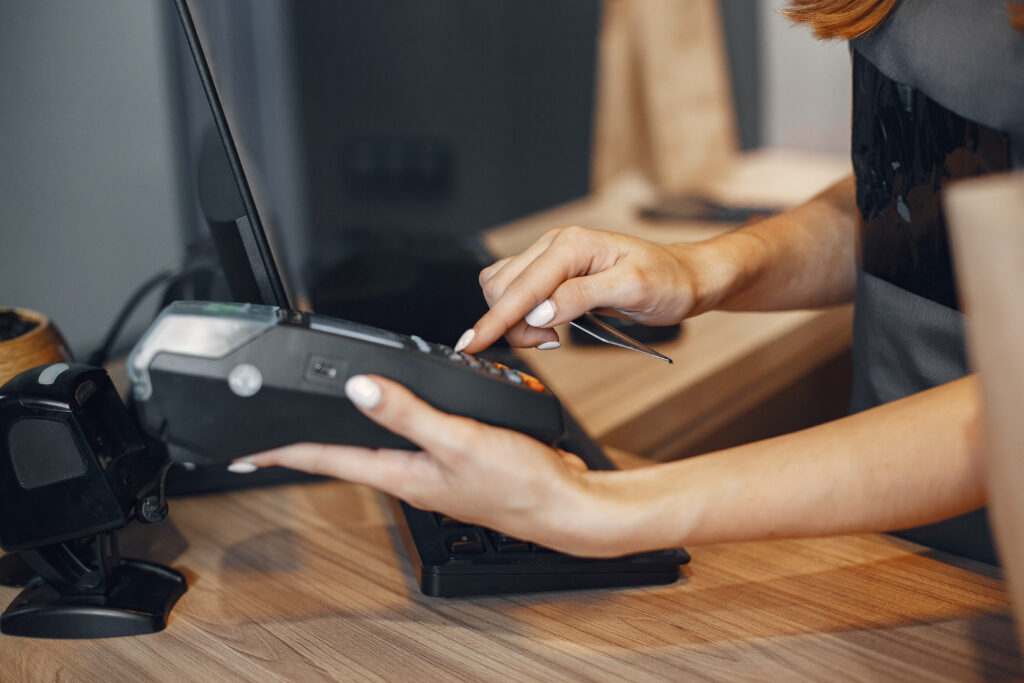 Close-up of a cashier using a credit card payment terminal at a checkout counter.