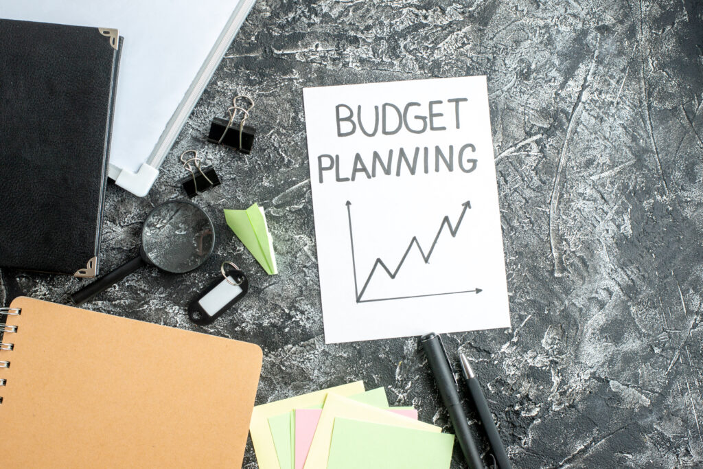 Top-down view of office supplies surrounding a card labeled Budget Planning with an upward line graph.