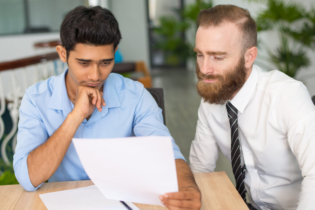 Two businessmen attentively reviewing a printed document together at a meeting desk.