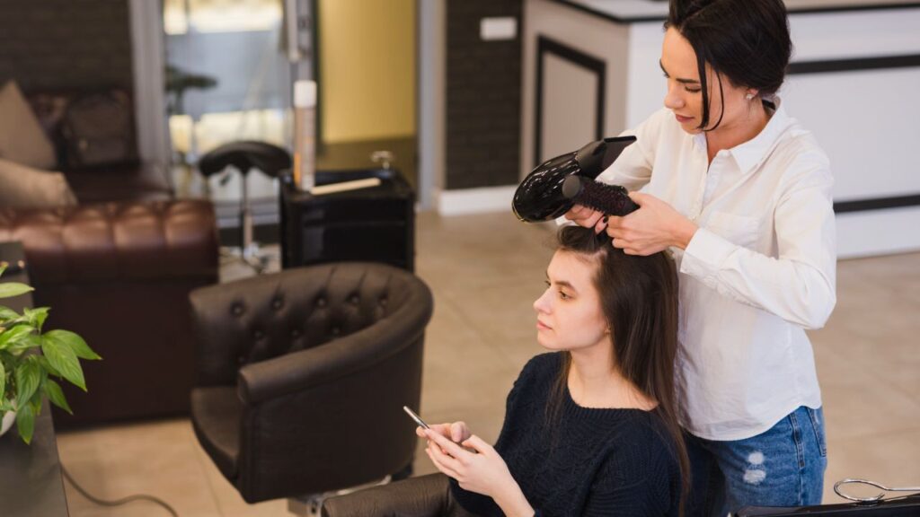 Professional hairstylist blow-drying and styling a client’s hair inside a modern beauty salon.