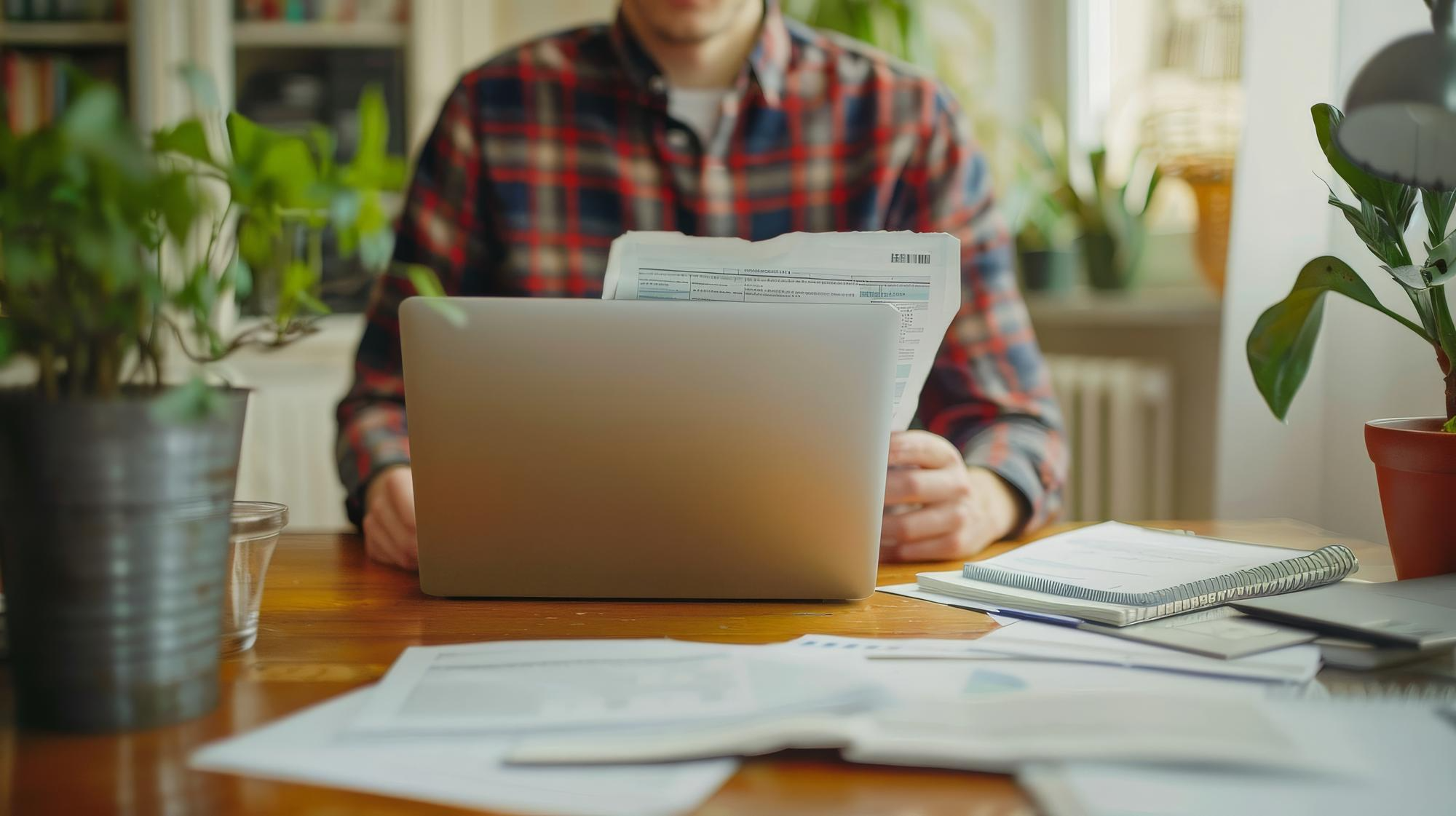 Small business owner reviewing tax documents and financial paperwork on a laptop while managing bookkeeping and accounting records.