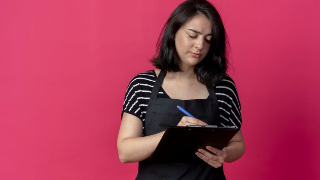 Salon owner reviewing business records on a clipboard while managing daily finances, bookkeeping, and operational expenses.