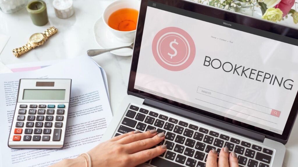 Laptop displaying bookkeeping software beside a calculator and financial documents.