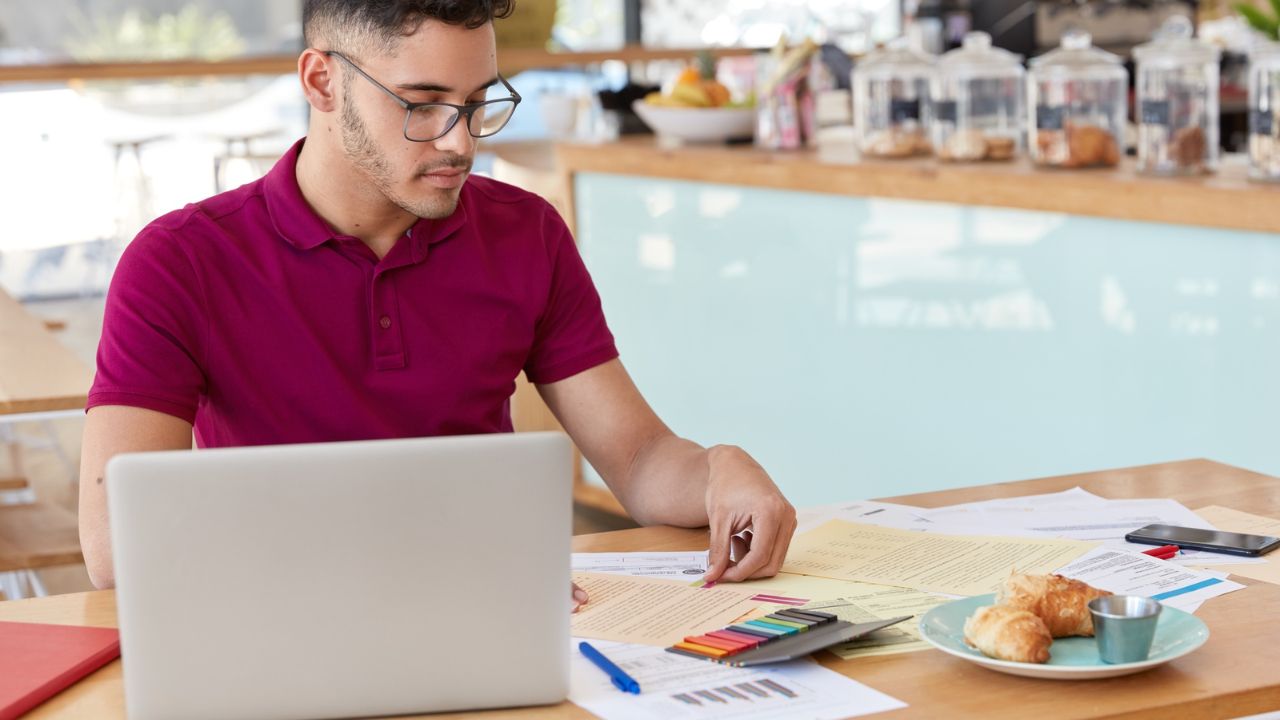 Small business owner reviewing financial documents, reports, and calculations on a laptop while managing business accounting.